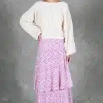 KELIS batwing top sewing pattern rear studio view: cream-white blouse with long loose sleeves worn over a pink-and-lilac tiered floral skirt.