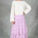 KELIS easy batwing blouse sewing pattern in a side three-quarter pose, with the cream long-sleeved top tucked into a lilac printed tiered skirt.