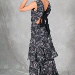 FOYS sewing pattern: three-quarter rear view of the FOYS evening dress sewing pattern in dark floral fabric, revealing the open back, black bow and flowing skirt tiers.