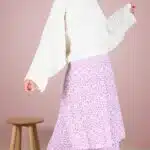 KELIS batwing top sewing pattern lifestyle image with a cream loose-sleeved blouse paired with a lilac printed tiered skirt in a pale pink studio.