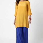 Loose-fit tunic sewing pattern MERVEILLE: smiling front view, yellow round-neck tunic and blue pants