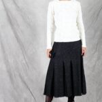 A woman is wearing a white top and a flared skirt with pleats crafted with a flared skirt sewing pattern.