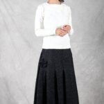 A woman is dressed in a white top paired with a pleated, flared skirt made using a flared skirt sewing pattern.