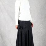 A woman is dressed in a white top paired with a pleated, flared skirt made using a flared skirt sewing pattern.