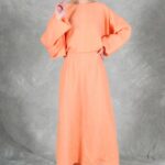 LOVY maxi dress sewing pattern in coral fabric: loose batwing sleeve, waist shaping and a full skirt in a standing pose.