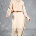 Front view of the LOVY batwing dress sewing pattern in cream fabric, with outstretched arms and a dark belt at the waist.