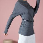 Top sewing pattern TWYS: charcoal grey long-sleeve top with draped collar, belted over a white skirt, pink backdrop