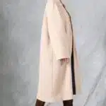 VIVIANE long coat sewing pattern: model in a beige coat with brown knee-high boots, standing against a pale grey backdrop.