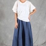 CALYS loose top sewing pattern front three-quarter photograph: model wearing a white draped short-sleeved blouse with a long navy skirt and white trainers.