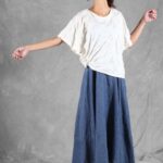 CALYS batwing-style top sewing pattern photographed with the model extending both arms, emphasizing the loose white sleeves and softly draped side seams.