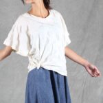 CALYS casual top sewing pattern medium shot, showing the white blouse tied into a side knot at the waist and its relaxed wide sleeves.