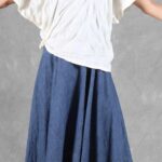 CALYS loose-fit top sewing pattern photographed from chest to hem with both arms outstretched to show the generous white sleeves above a blue skirt.