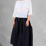 Mannequin portant un haut ample pour femme avec des manches trois-quarts, confectionné à partir d'un patron de couture. Le tissu est léger et semi-transparent, avec un motif floral délicat, associé à une longue jupe volumineuse de couleur noire pour un look élégant et fluide.