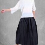 Mannequin portant un haut ample pour femme avec des manches trois-quarts, confectionné à partir d'un patron de couture. Le tissu est léger et semi-transparent, avec un motif floral délicat, associé à une longue jupe volumineuse de couleur noire pour un look élégant et fluide.