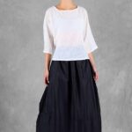 Mannequin portant un haut ample pour femme avec des manches trois-quarts, confectionné à partir d'un patron de couture. Le tissu est léger et semi-transparent, avec un motif floral délicat, associé à une longue jupe volumineuse de couleur noire pour un look élégant et fluide.