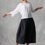 Mannequin portant un haut ample pour femme avec des manches trois-quarts, confectionné à partir d'un patron de couture. Le tissu est léger et semi-transparent, avec un motif floral délicat, associé à une longue jupe volumineuse de couleur noire pour un look élégant et fluide.