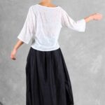 Mannequin portant un haut ample pour femme avec des manches trois-quarts, confectionné à partir d'un patron de couture. Le tissu est léger et semi-transparent, avec un motif floral délicat, associé à une longue jupe volumineuse de couleur noire pour un look élégant et fluide.
