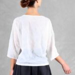 Mannequin portant un haut ample pour femme avec des manches trois-quarts, confectionné à partir d'un patron de couture. Le tissu est léger et semi-transparent, avec un motif floral délicat, associé à une longue jupe volumineuse de couleur noire pour un look élégant et fluide.