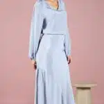 GIULIA sewing pattern: gIULIA bias-cut midi skirt sewing pattern in pale blue, worn with a matching blouse; the model poses before a pink wall with the side ruffle visible.
