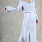 GIULIA sewing pattern: gIULIA midi skirt sewing pattern worn in pale blue fabric, seen full length as the model steps sideways with an outstretched arm and draped lower hem.