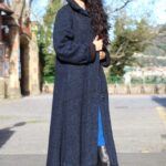 Model wearing a long coat made from the LOOMYS hooded coat sewing pattern, with a generous hood, a softly fitted upper body and a gently flared hem.