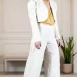 MINIMALISTE wide-leg pants sewing pattern: model in high-waisted textured cream trousers, cropped ivory jacket and mustard satin top, photographed against a grey background.