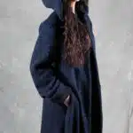 Modelo vistiendo un abrigo largo con capucha, confeccionado con un patrón de abrigo con capucha, que muestra un diseño semiajustado, con vuelo y cierre de botones.