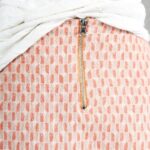 AVA box-pleat skirt sewing pattern close-up: exposed centre-back zipper in peach-pink geometric fabric, with the white top lifted to reveal the skirt fastening.