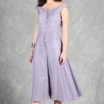 A woman with long dark hair stands in front of a grey backdrop wearing a lavender, button-down, midi-length dress crafted with a summer dress pattern.