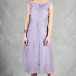 A woman stands against a grey backdrop, wearing a light purple, sleeveless, button-down dress crafted with a summer dress pattern that falls to mid-calf.