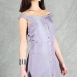 A woman with long dark hair stands against a gray background. She is wearing an off-shoulder, sleeveless lavender dress crafted with a summer dress pattern.