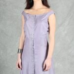 A woman stands in front of a gray textured backdrop, wearing a sleeveless light purple dress crafted with a summer dress pattern.