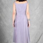 A woman stands with her back to the camera, wearing a lavender, sleeveless, knee-length dress crafted with a summer dress pattern.
