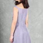 A woman with shoulder-length dark hair stands with her back to the camera, slightly turning her head over her left shoulder. She is wearing a sleeveless, floor-length, light lavender dress made with a summer dress pattern.