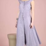IRIS summer dress sewing pattern product photograph: lilac button-front midi dress with draped shoulder straps and an A-line skirt, model standing against a soft pink backdrop.
