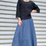 A woman wearing a loose long-sleeve black top and a flowing blue ankle-length skirt crafted with a boho pattern.