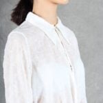 A woman is wearing a sheer white shirt with floral embroidery, crafted with a shirt sewing pattern.