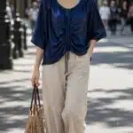 MAR ruched top sewing pattern: navy-blue gathered blouse with central drawstring, worn outdoors with light beige trousers.