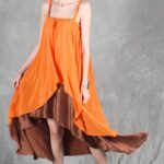 Model wearing a flowing top and skirt with an asymmetrical hem, made from a top and skirt sewing pattern. The orange top drapes elegantly over a brown skirt with a satin finish, creating a layered effect.