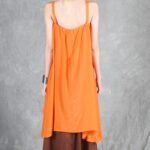 Model wearing a flowing top and skirt with an asymmetrical hem, made from a top and skirt sewing pattern. The orange top drapes elegantly over a brown skirt with a satin finish, creating a layered effect.