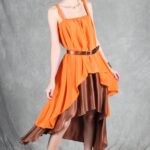 Model wearing a flowing top and skirt with an asymmetrical hem, made from a top and skirt sewing pattern. The orange top drapes elegantly over a brown skirt with a satin finish, creating a layered effect.