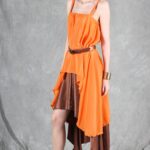 Model wearing a flowing top and skirt with an asymmetrical hem, made from a top and skirt sewing pattern. The orange top drapes elegantly over a brown skirt with a satin finish, creating a layered effect.