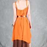 Model wearing a flowing top and skirt with an asymmetrical hem, made from a top and skirt sewing pattern. The orange top drapes elegantly over a brown skirt with a satin finish, creating a layered effect.