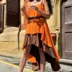 Model wearing a flowing top and skirt with an asymmetrical hem, made from a top and skirt sewing pattern. The orange top drapes elegantly over a brown skirt with a satin finish, creating a layered effect.