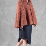 Woman wearing a cozy brown cape, crafted with a ladies cape pattern, featuring a rounded collar and a decorative brooch for closure.