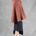 Woman wearing a cozy brown cape, crafted with a ladies cape pattern, featuring a rounded collar and a decorative brooch for closure.
