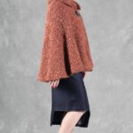 Woman wearing a cozy brown cape, crafted with a ladies cape pattern, featuring a rounded collar and a decorative brooch for closure.