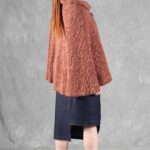 Woman wearing a cozy brown cape, crafted with a ladies cape pattern, featuring a rounded collar and a decorative brooch for closure.
