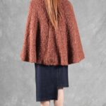 Woman wearing a cozy brown cape, crafted with a ladies cape pattern, featuring a rounded collar and a decorative brooch for closure.