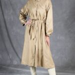 BLIZZARD belted raincoat sewing pattern, front view of a beige coat with a relaxed fit and one hand resting on the waist.